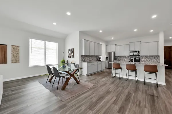 a living room with stainless steel appliances furniture wooden floor and a kitchen view
