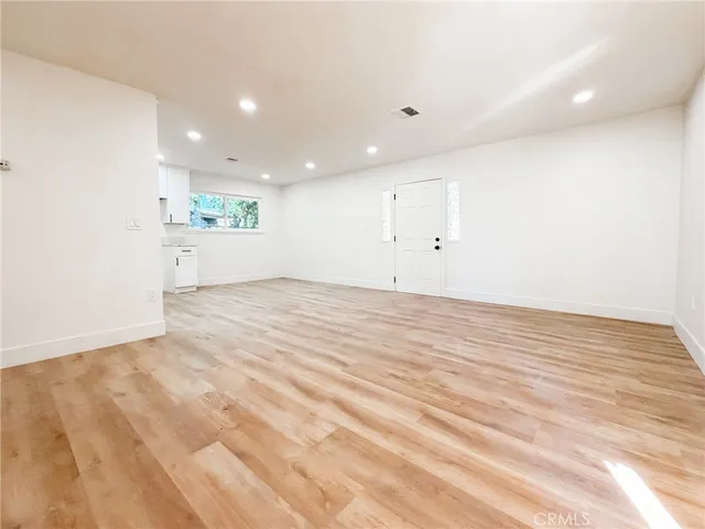 a view of an empty room with wooden floor and kitchen