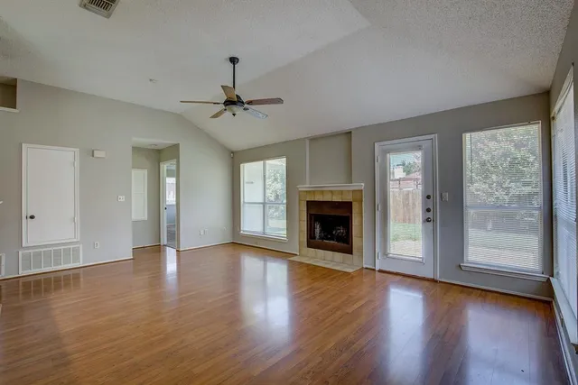 an empty room with wooden floor fireplace and windows