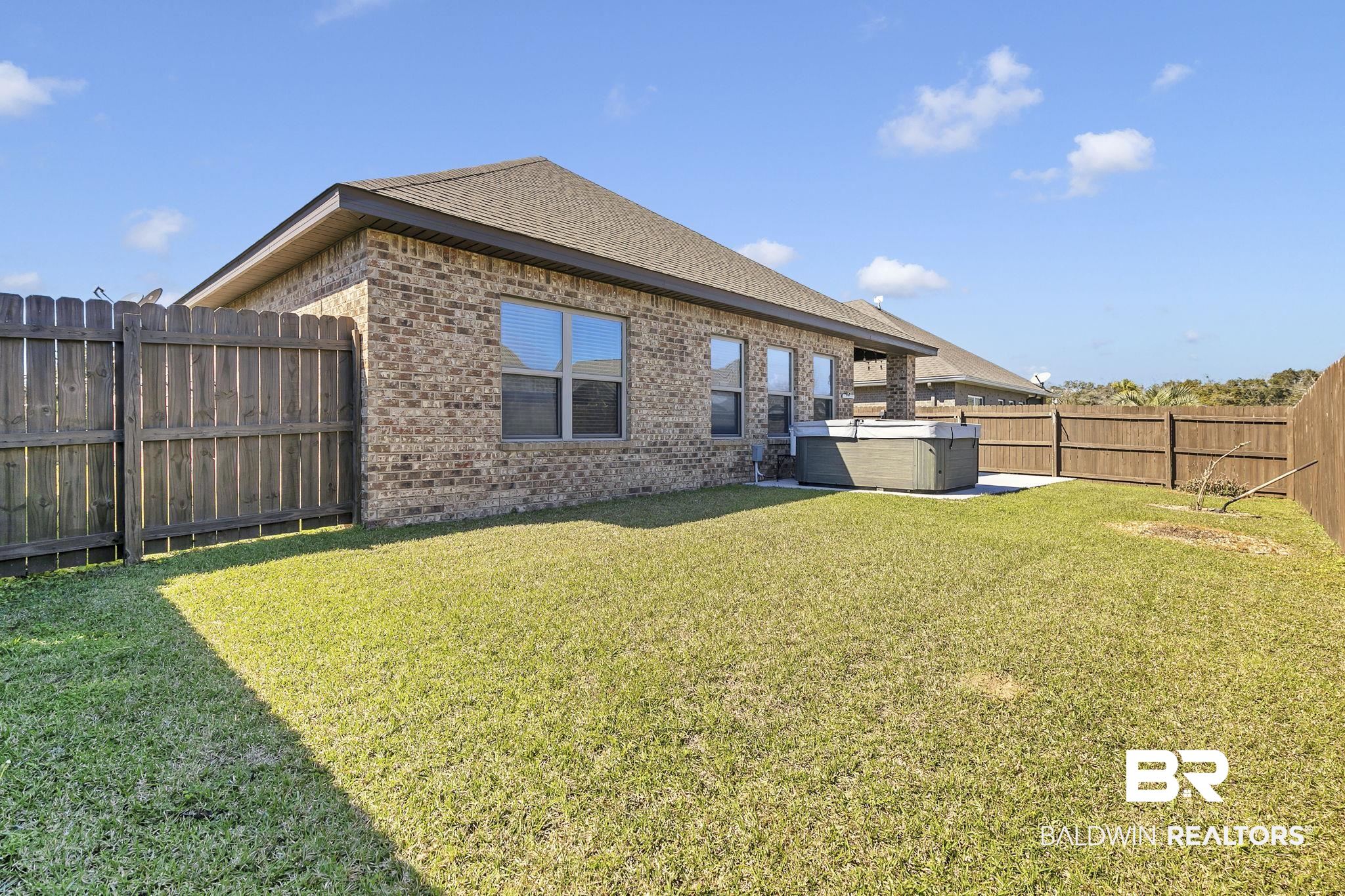 1547 Kairos Loop Foley, AL 36535 - Photo 36 of 55 Rear view of property with a fenced backyard, brick siding, roof with shingles, a lawn, and a hot tub