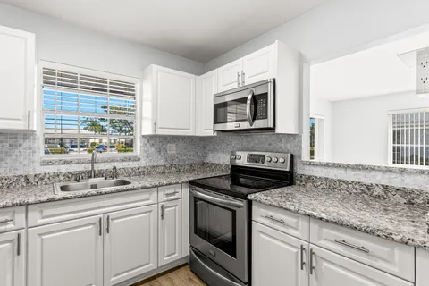 a kitchen with granite countertop white cabinets white appliances a sink and a window