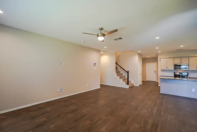 an empty room with wooden floor a ceiling fan and kitchen view