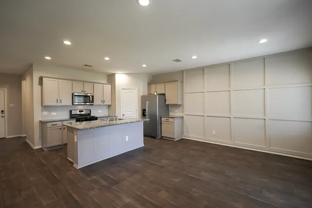 a large kitchen with stainless steel appliances granite countertop a large counter top a stove a sink and a refrigerator with wooden floor