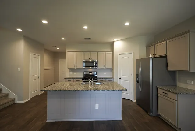 a kitchen with kitchen island granite countertop a refrigerator stove top oven and wooden floor