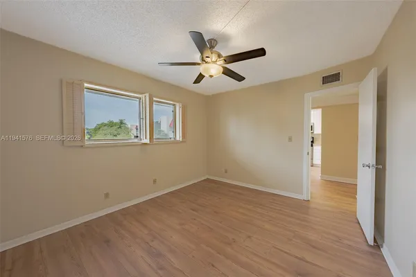 an empty room with wooden floor ceiling fan and windows