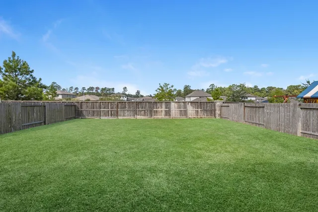 a view of a backyard with a huge green area and wooden fence