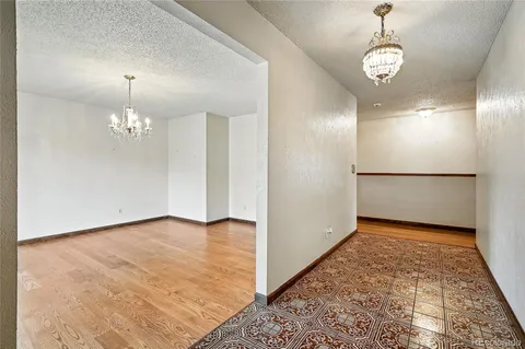 a view of an empty room with chandelier and kitchen view