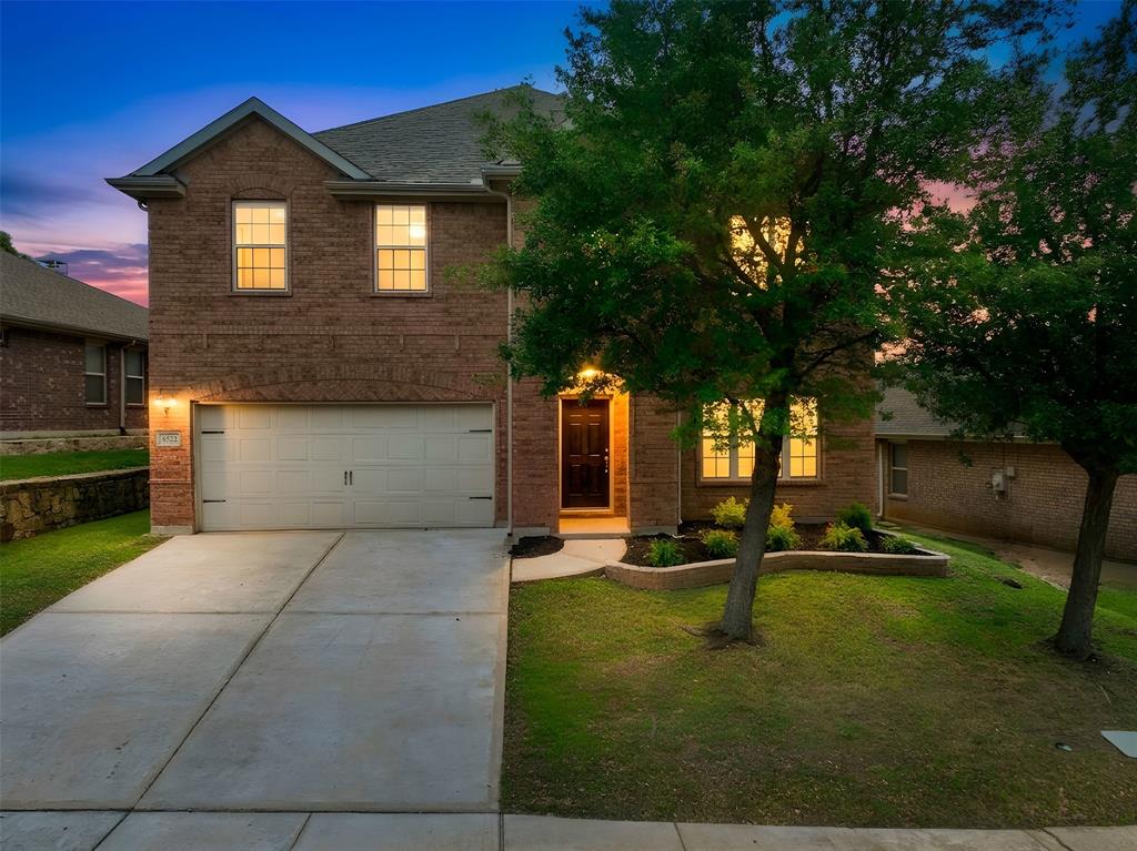 6522 Portside Ridge Lane Dallas, TX 75249 - Photo 1 of 37 Brick facade home featuring a two-car garage, concrete driveway, front entry with transom window, manicured lawn, and mature trees
