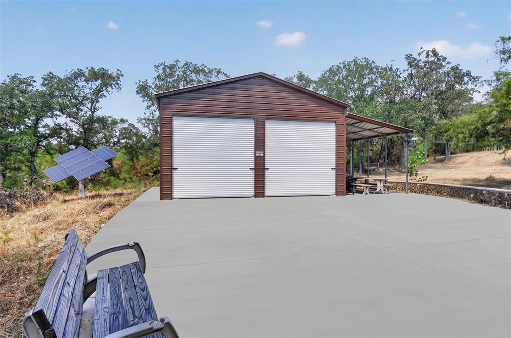 1623 3 Skillet Road Springtown, TX 76082 - Photo 39 of 40 Two-bay metal garage with roll-up doors, an attached covered patio, and concrete paving