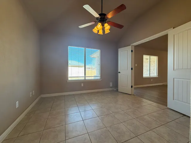 an empty room with a chandelier fan and windows