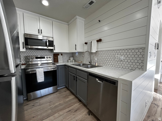 608 South 500 West, Unit 3 Provo, UT 84601 - Photo 11 of 35 Contemporary kitchen featuring stainless steel appliances, two-tone cabinetry with white upper and gray lower cabinets, hexagon tile backsplash, wood-finish flooring, and white shiplap wall paneling