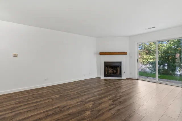 a view of an empty room with wooden floor fireplace and a window
