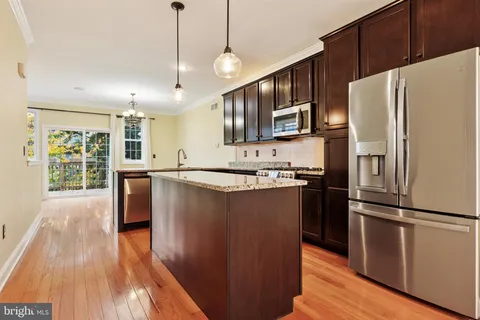 a kitchen with stainless steel appliances granite countertop a refrigerator a sink dishwasher a stove and white countertops with wooden floor