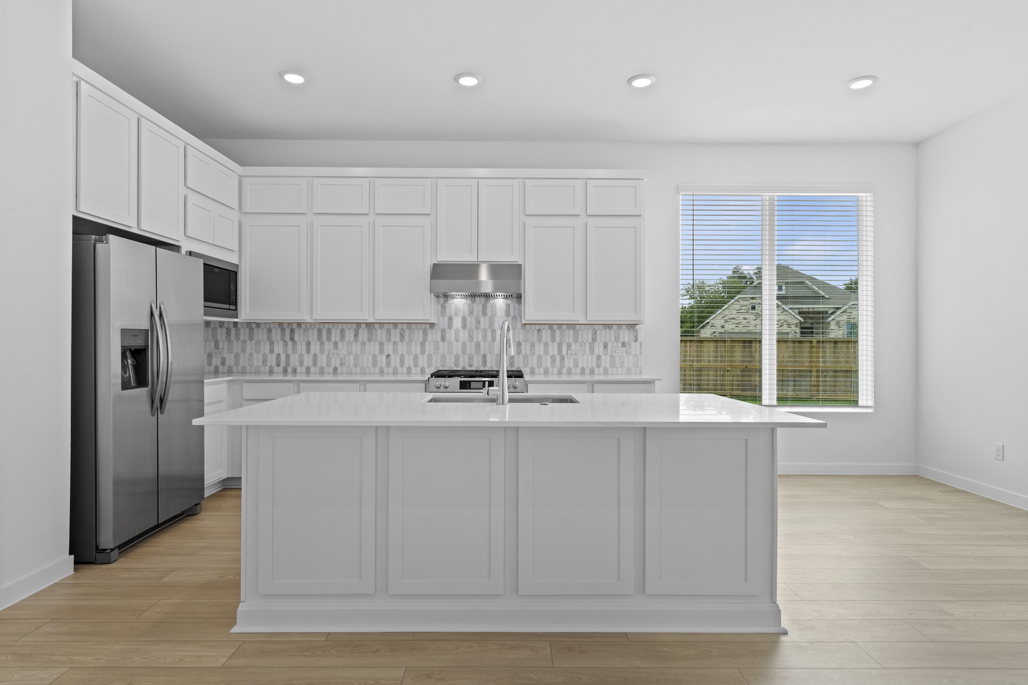 2720 Grove Crest Drive Rosenberg, TX 77469 - Photo 10 of 32 This modern kitchen features a spacious island with a sink, stainless steel appliances, and a stylish tile backsplash. Ample natural light flows through a large window, complementing the bright and airy atmosphere.