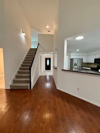 a view of an empty room with wooden floor and kitchen
