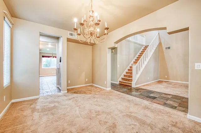 a view of an empty room with stairs and chandelier