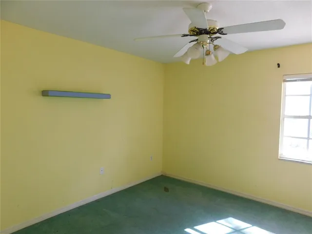 an empty room with chandelier fan and windows