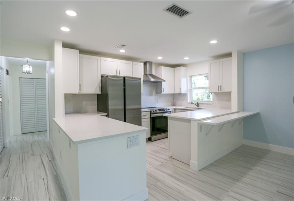 225 Georgetown Boulevard Naples, FL 34112 - Photo 21 of 37 Kitchen featuring appliances with stainless steel finishes, tasteful backsplash, white cabinetry, kitchen peninsula, and wall chimney exhaust hood