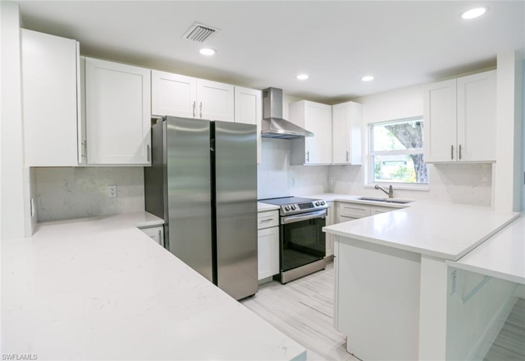 225 Georgetown Boulevard Naples, FL 34112 - Photo 22 of 37 Kitchen featuring decorative backsplash, white cabinets, wall chimney range hood, and appliances with stainless steel finishes