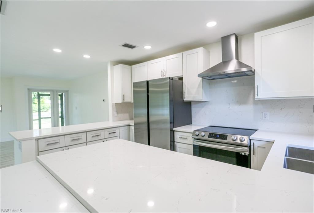 225 Georgetown Boulevard Naples, FL 34112 - Photo 23 of 37 Kitchen with wall chimney exhaust hood, light stone counters, kitchen peninsula, and appliances with stainless steel finishes