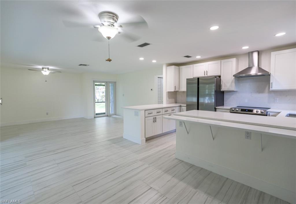 225 Georgetown Boulevard Naples, FL 34112 - Photo 24 of 37 Kitchen featuring wall chimney range hood, kitchen peninsula, white cabinets, and appliances with stainless steel finishes