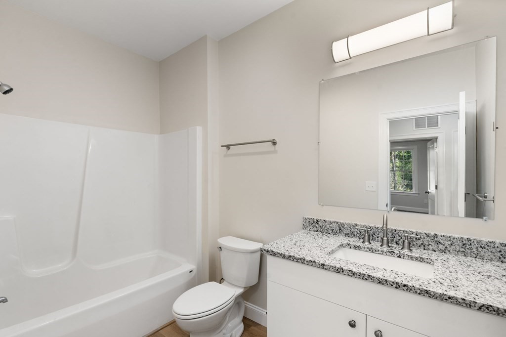 242 Main Street, Unit 103 Millis, MA 02054 - Photo 12 of 18 a bathroom with a granite countertop sink a toilet and bathtub