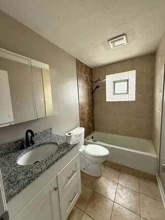 a bathroom with a granite countertop sink a toilet a mirror and bathtub
