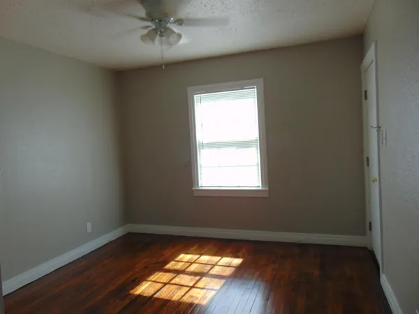 an empty room with wooden floor chandelier fan and windows