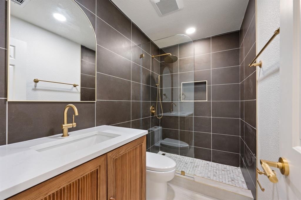 6403 Genstar Lane Dallas, TX 75252 - Photo 26 of 34 Contemporary bathroom featuring a wood-panel vanity with integrated sink, a gold-finish faucet, and an arched mirror