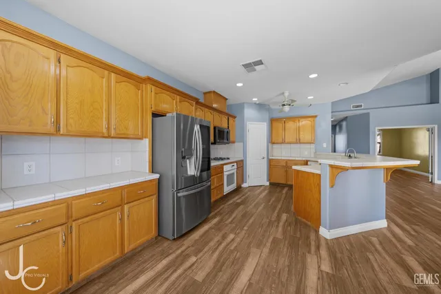 a kitchen with stainless steel appliances granite countertop a refrigerator a sink dishwasher and wooden cabinets with wooden floor