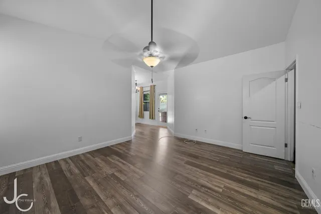 a view of an empty room with chandelier fan and wooden floor