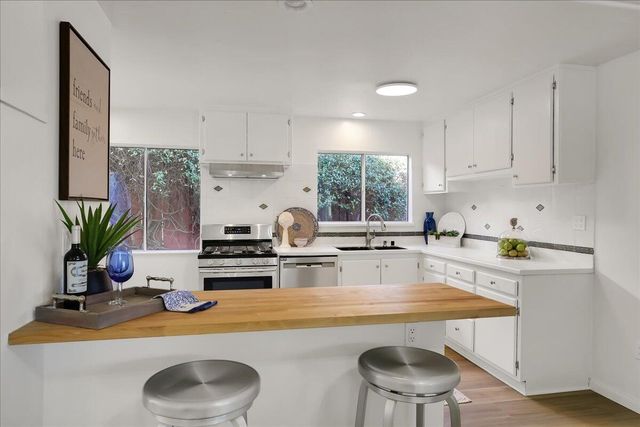 a kitchen with kitchen island a stove a sink a refrigerator and white cabinets with wooden floor