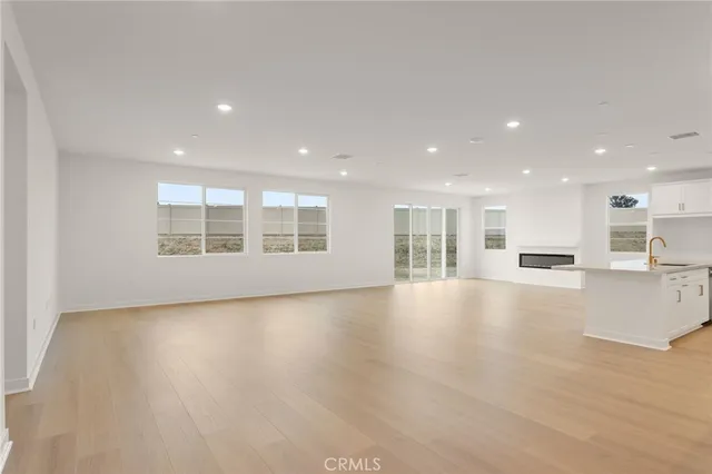 a view of an empty room with wooden floor and a kitchen