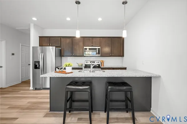 a kitchen with stainless steel appliances granite countertop a sink a stove a refrigerator and island with wooden floor