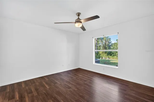 an empty room with wooden floor ceiling fan and windows