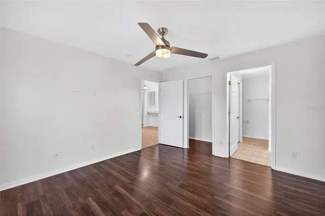 a view of an empty room with wooden floor and a ceiling fan
