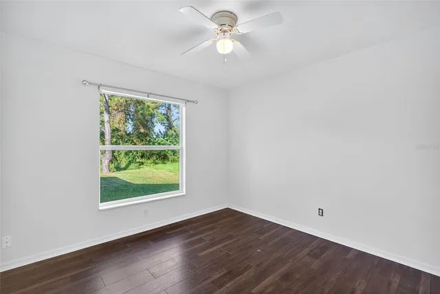 an empty room with wooden floor chandelier fan and windows