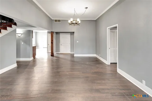 a view of an empty room with wooden floor and a chandelier