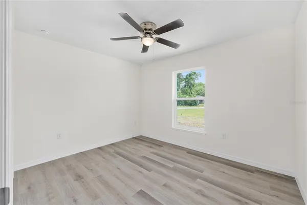 an empty room with wooden floor ceiling fan and windows