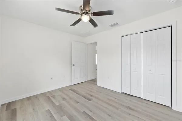 an empty room with wooden floor closet and fan
