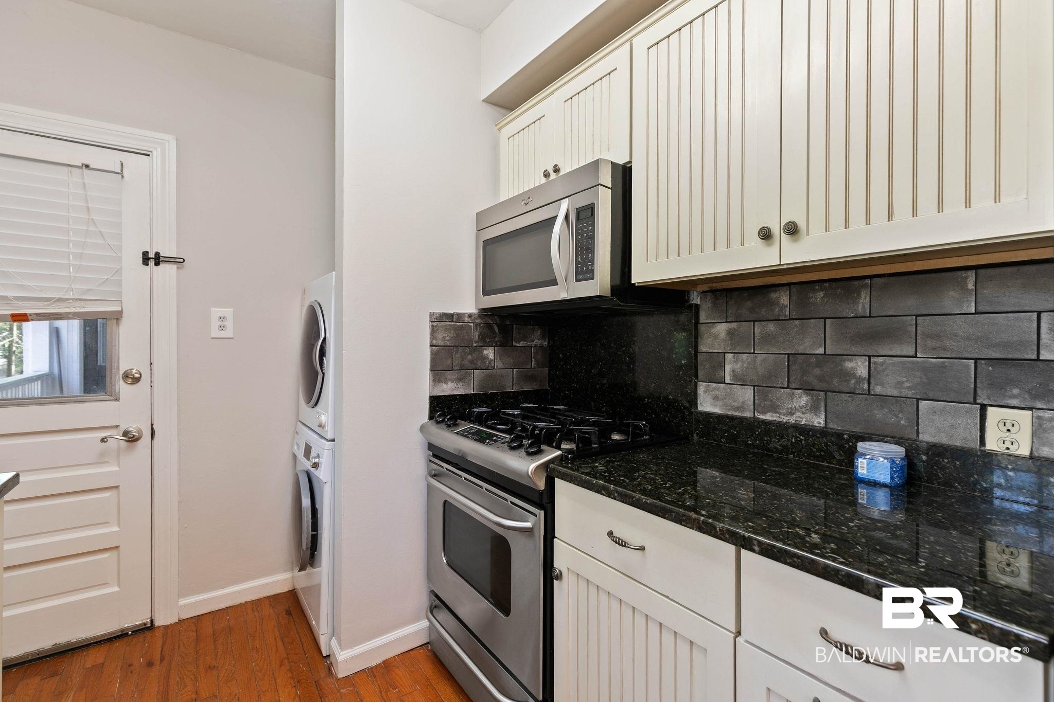 214 Upham Street, Unit 8D Mobile, AL 36607 - Photo 11 of 36 Kitchen with stainless steel appliances, light wood-style floors, tasteful backsplash, stacked washer / drying machine, and dark stone counters