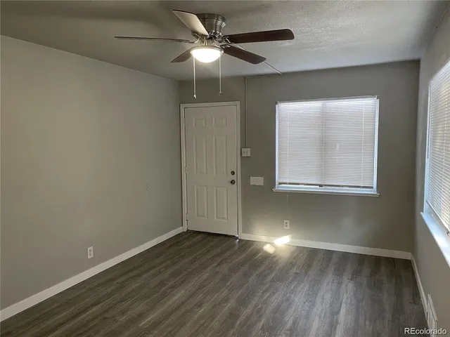 an empty room with wooden floor chandelier fan and windows