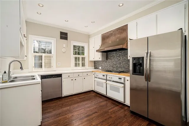 a kitchen with stainless steel appliances granite countertop a refrigerator a sink dishwasher a stove and white cabinets with wooden floor