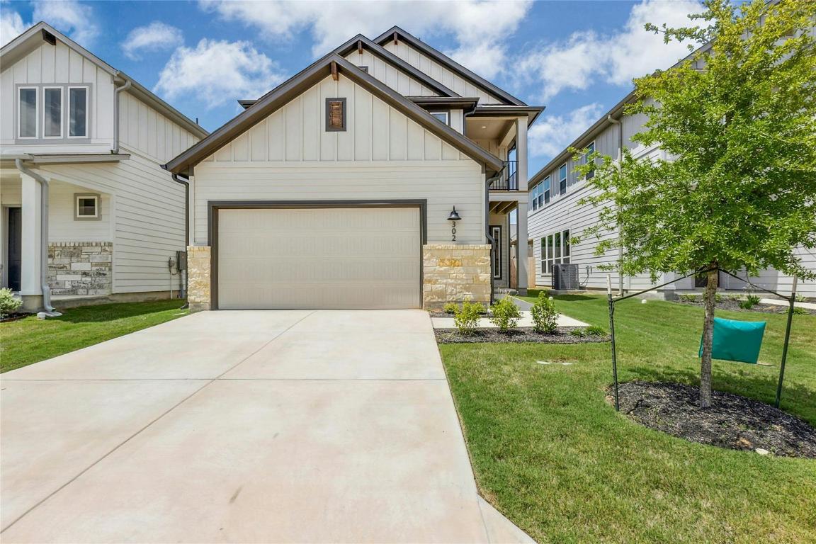 View of front of home with board and batten siding, a balcony, stone siding, concrete driveway, and a front yard