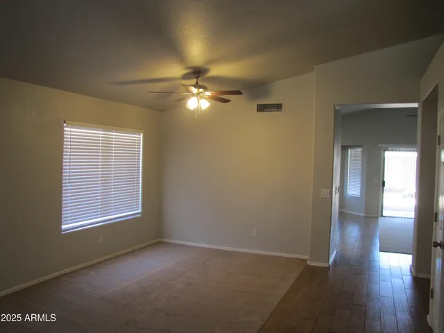 an empty room with wooden floor chandelier fan and windows