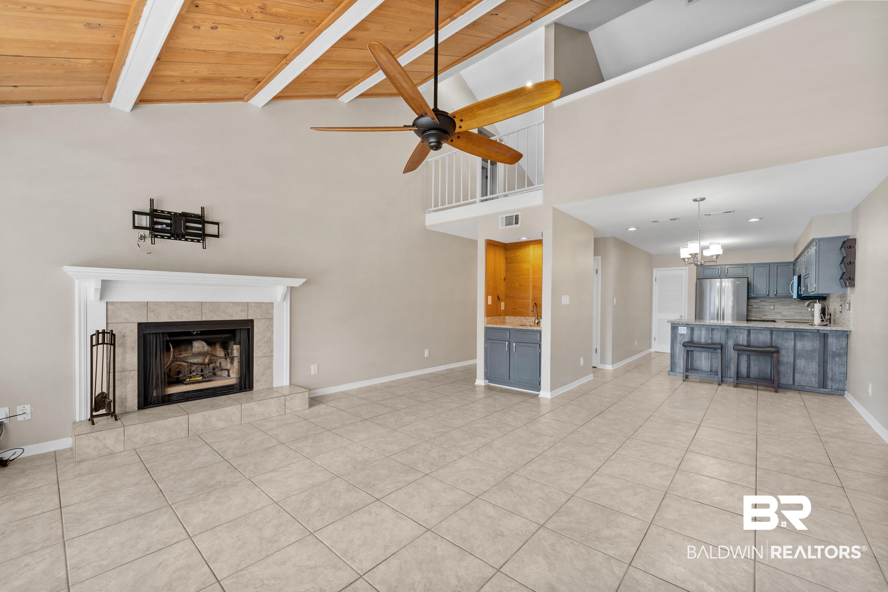 1701 Regency Road, Unit 111 Gulf Shores, AL 36542 - Photo 8 of 29 Unfurnished living room with wood ceiling, a tiled fireplace, light tile patterned flooring, and ceiling fan with notable chandelier