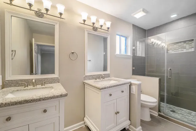 a bathroom with a granite countertop sink a toilet a mirror and shower