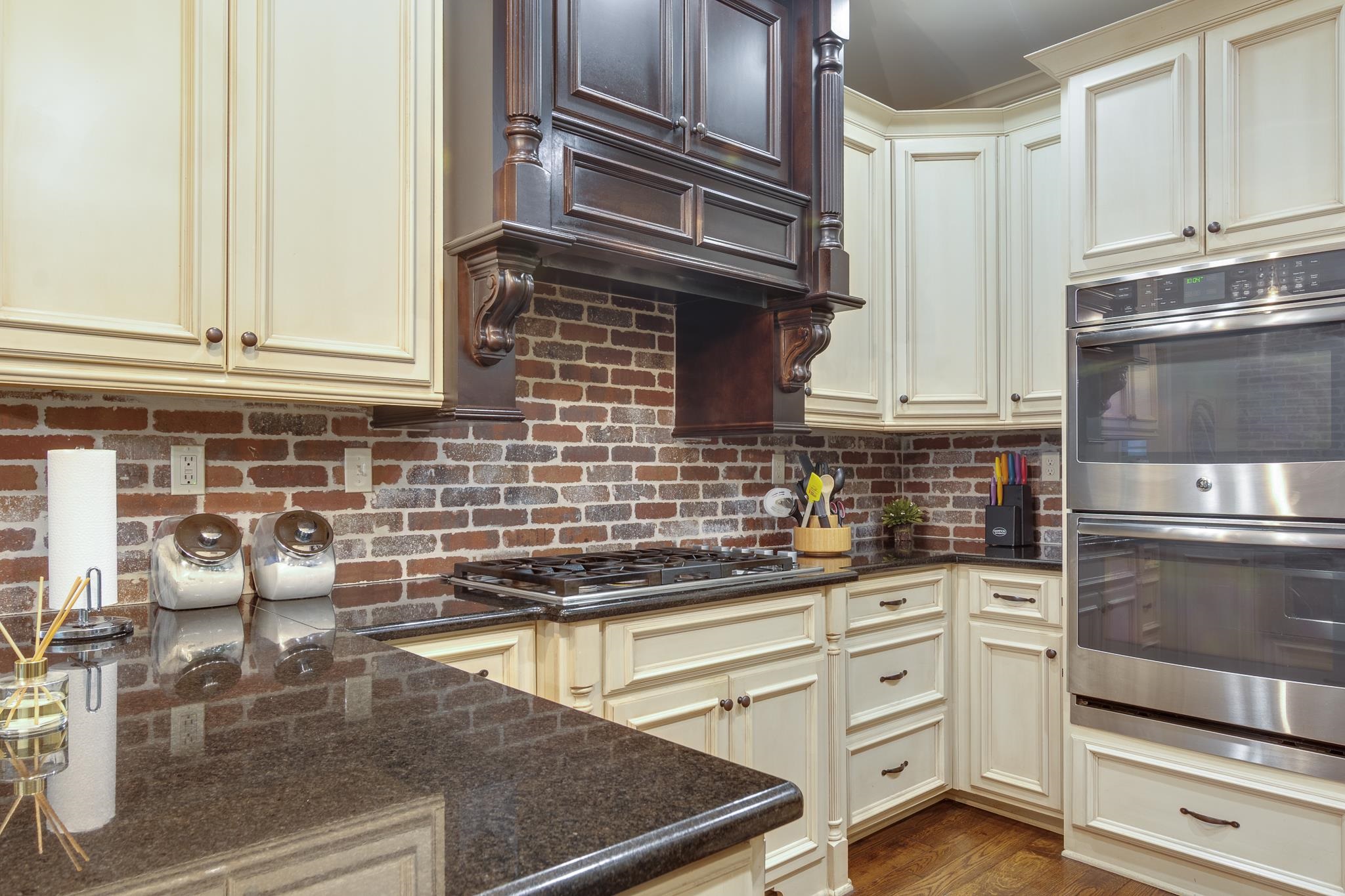 791 North Tree Drive Collierville, TN 38017 - Photo 6 of 27 Kitchen featuring cream-toned cabinetry, dark wood-finish range hood, brick-look backsplash, dark countertops, and stainless steel double ovens