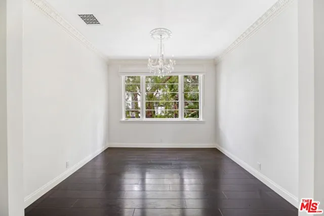 an empty room with wooden floor chandelier and windows