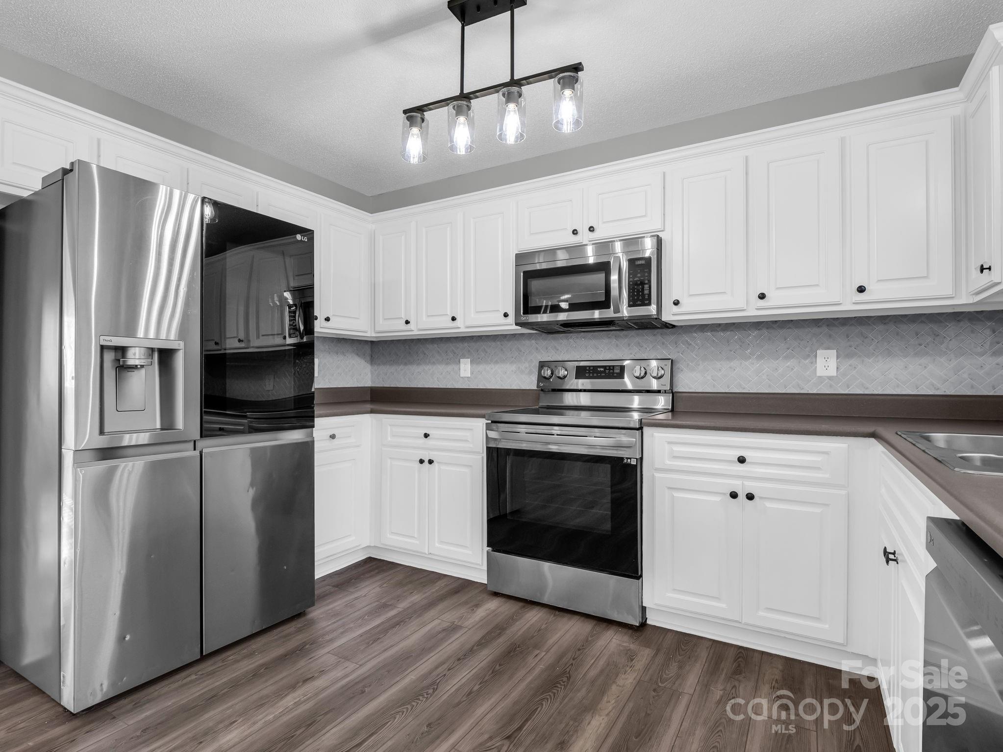 340 Sarratt Creek Road Gaffney, SC 29341 - Photo 14 of 46 a kitchen with stainless steel appliances white cabinets a sink a stove a refrigerator and microwave with wooden floor
